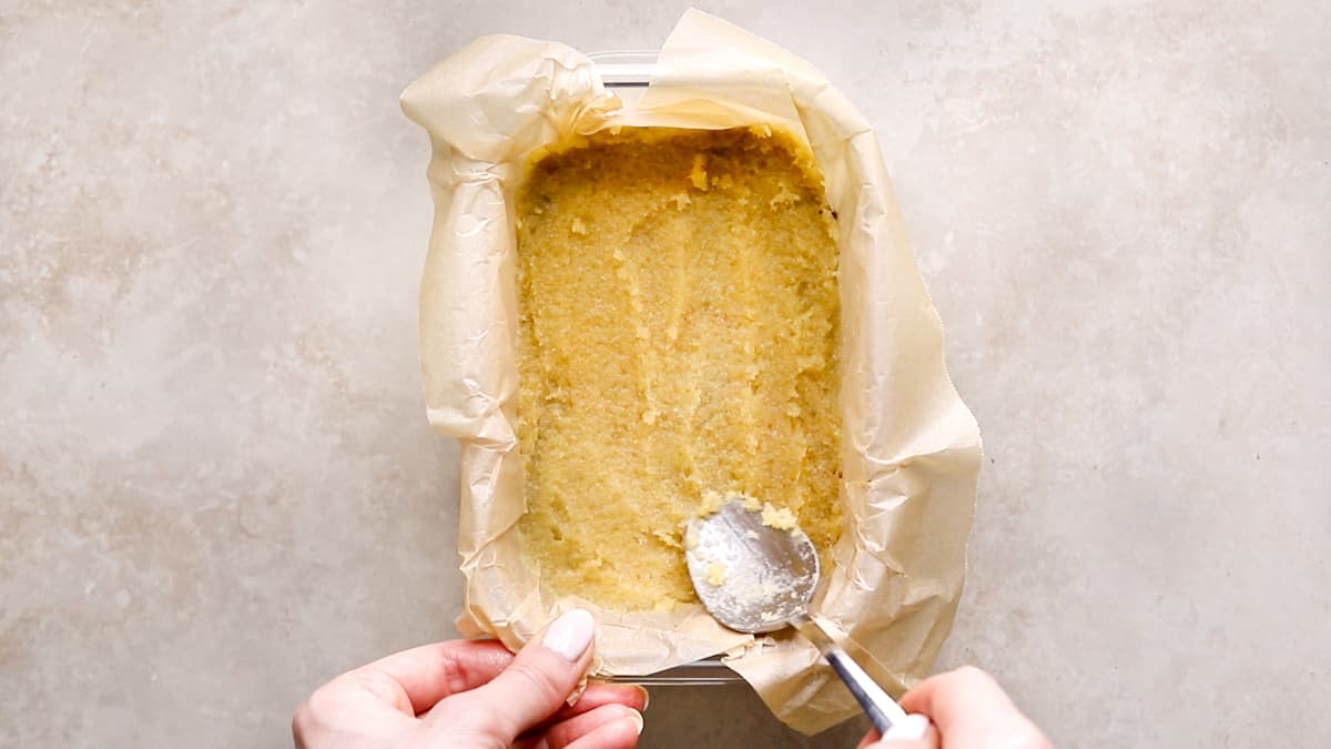 A teaspoon spreading crystallized ginger paste evenly over the chocolate biscuit base