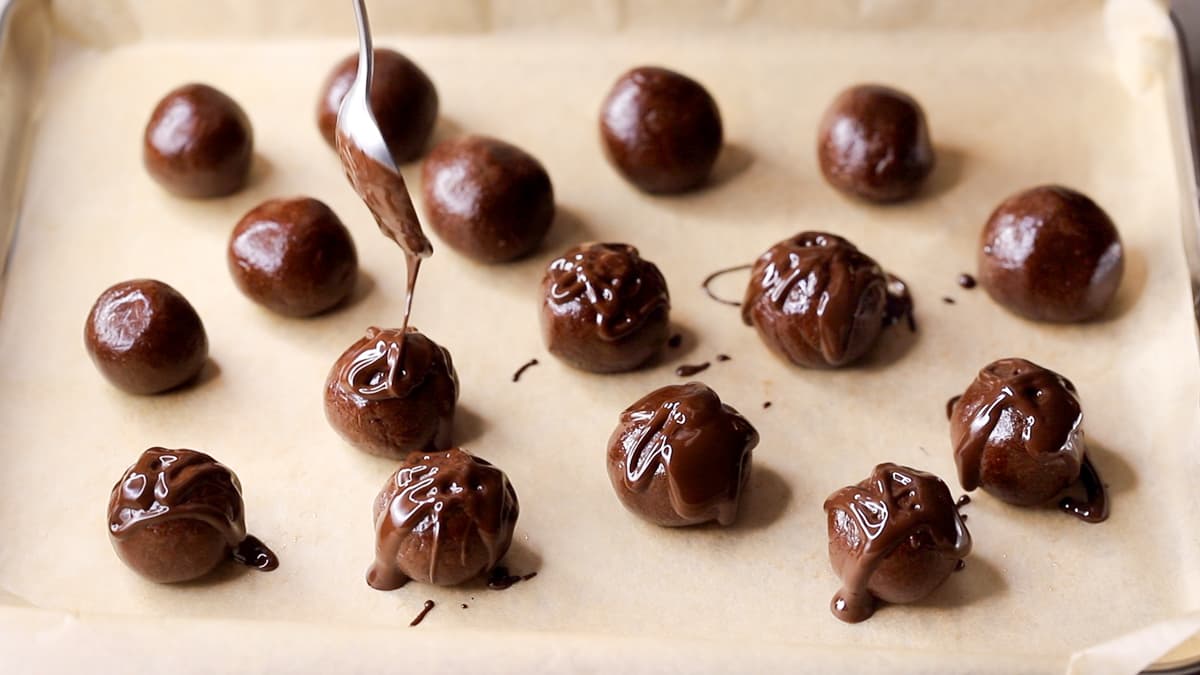 Melted dark chocolate being drizzled over choc mint protein balls on a tray
