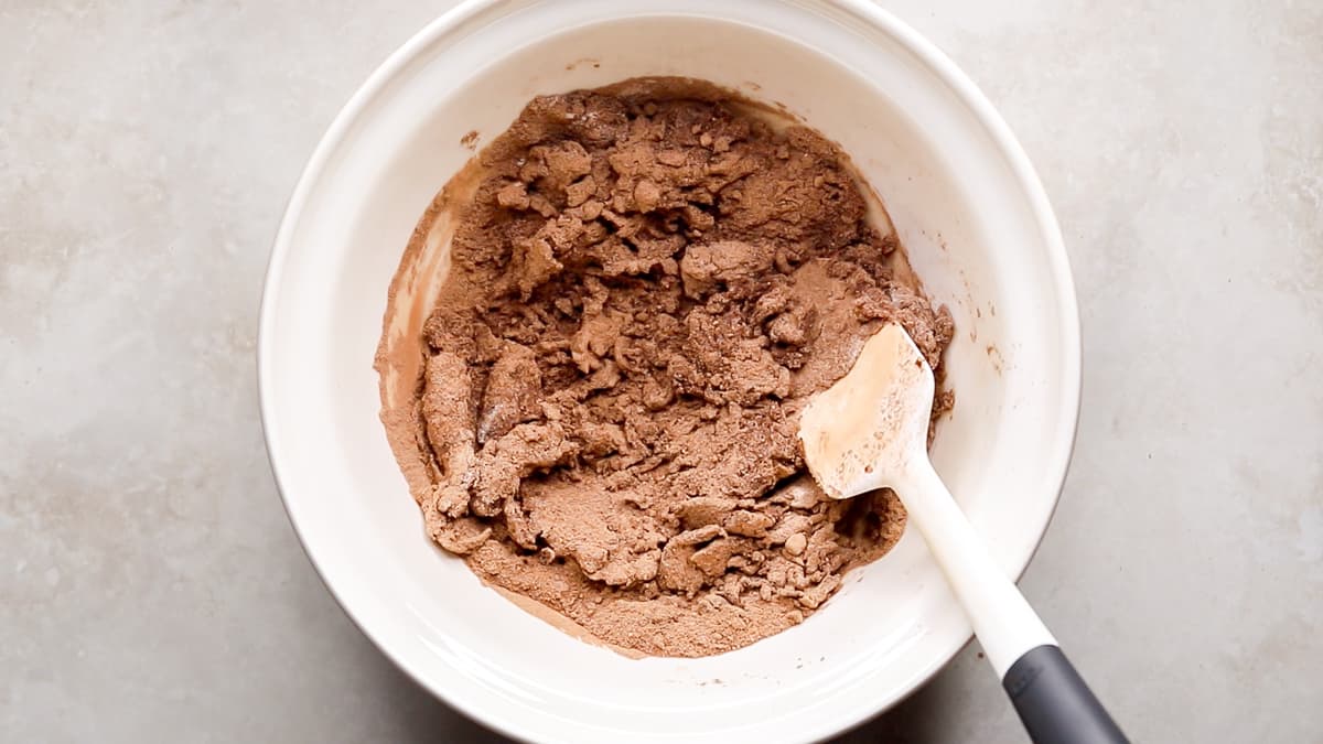 Mixing bowl with protein, almond butter, cacao, and coconut flour being stirred
