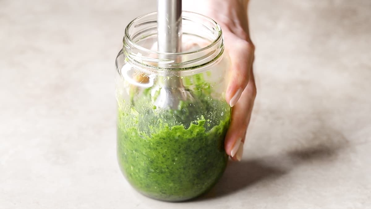 Parsley, pine nuts, Parmesan, garlic, olive oil, and salt in a jar being blended with a hand blender to make pesto