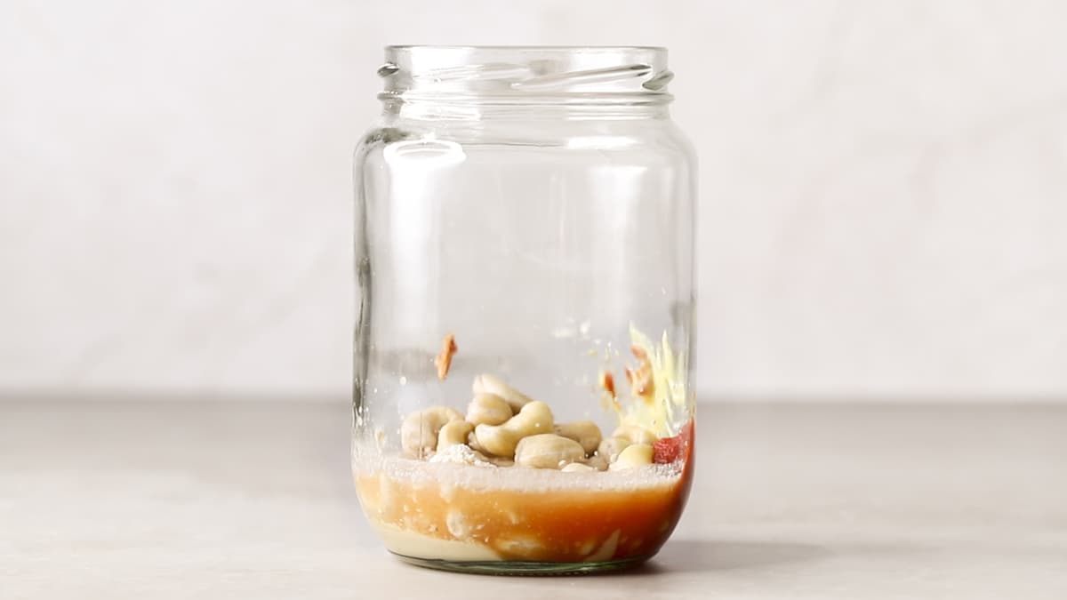 A glass jar containing cashew nuts and other sauce ingredients