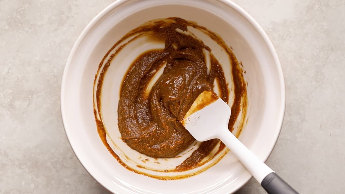 A mixing bowl with cashew butter, maple syrup, vanilla, dissolved coffee, and salt being stirred together with a spatula