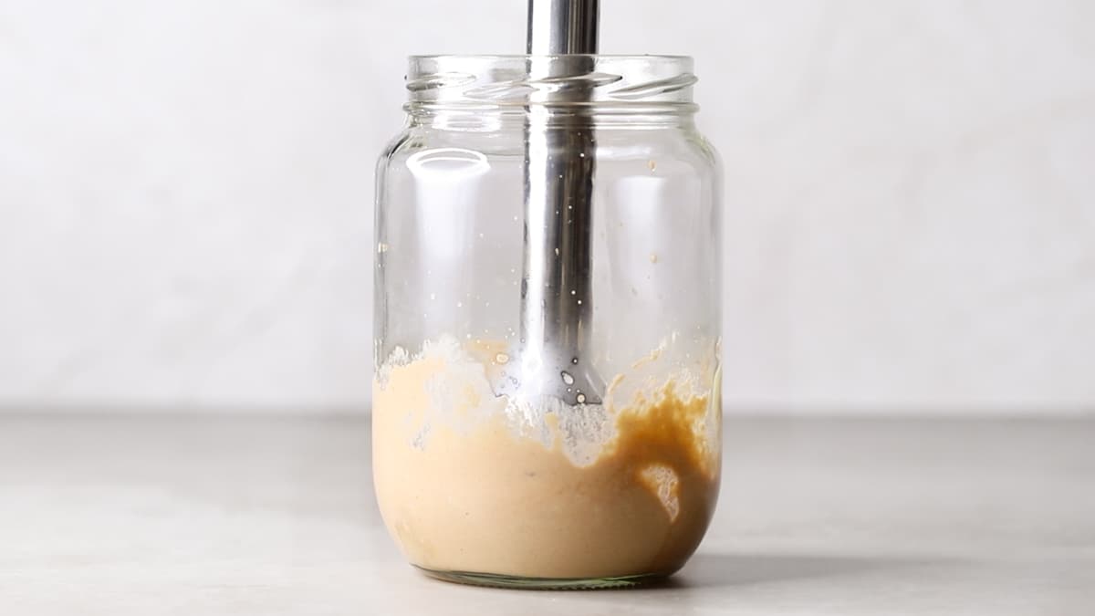 Hand blender inside a jar blending sauce ingredients into a smooth consistency