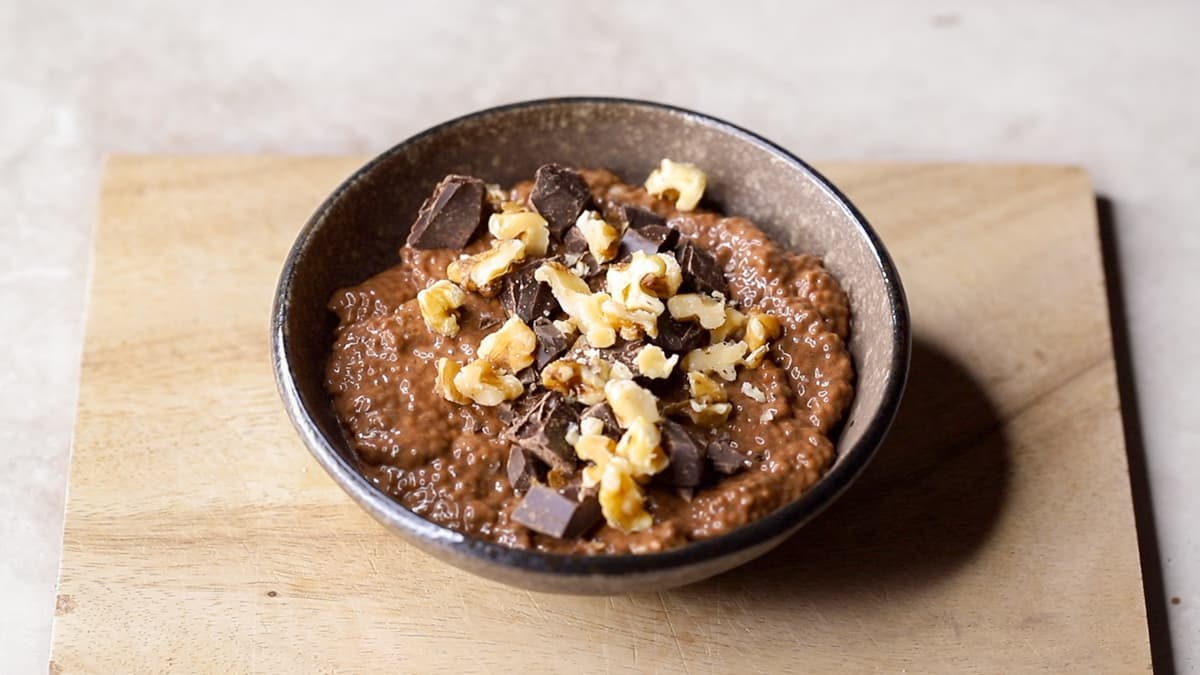 A serving of chocolate chia pudding in a bowl, topped with chopped walnuts, and dark chocolate
