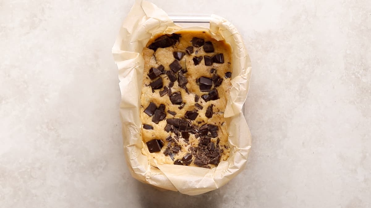 Cookie dough protein bar mixture pressed into lined container with chocolate chips on top
