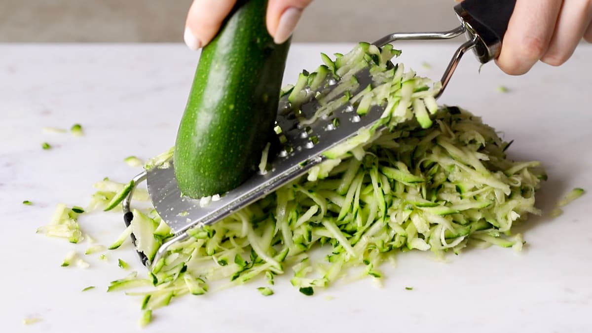 Zucchini being grated on a chopping board with a handheld grater