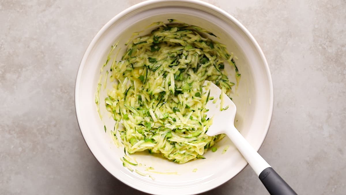 A bowl containing grated zucchini mixed with eggs and olive oil