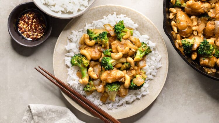 Easy gluten-free cashew chicken with broccoli served on a plate with white rice and chili flakes