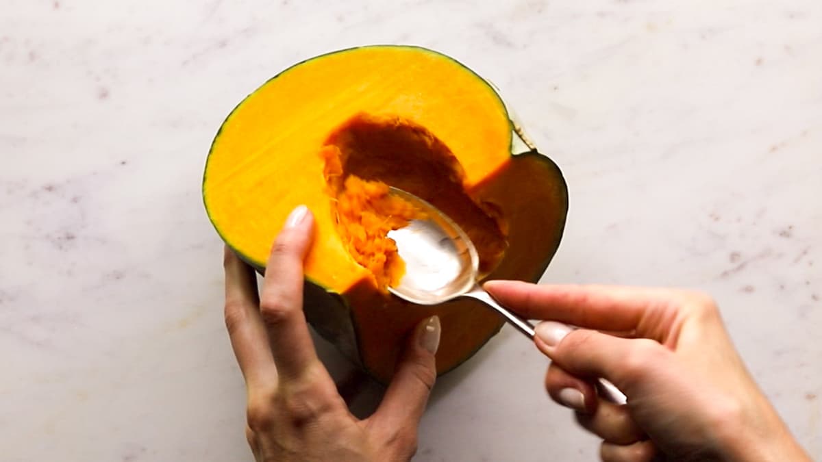 Spoon scooping seeds from halved pumpkin