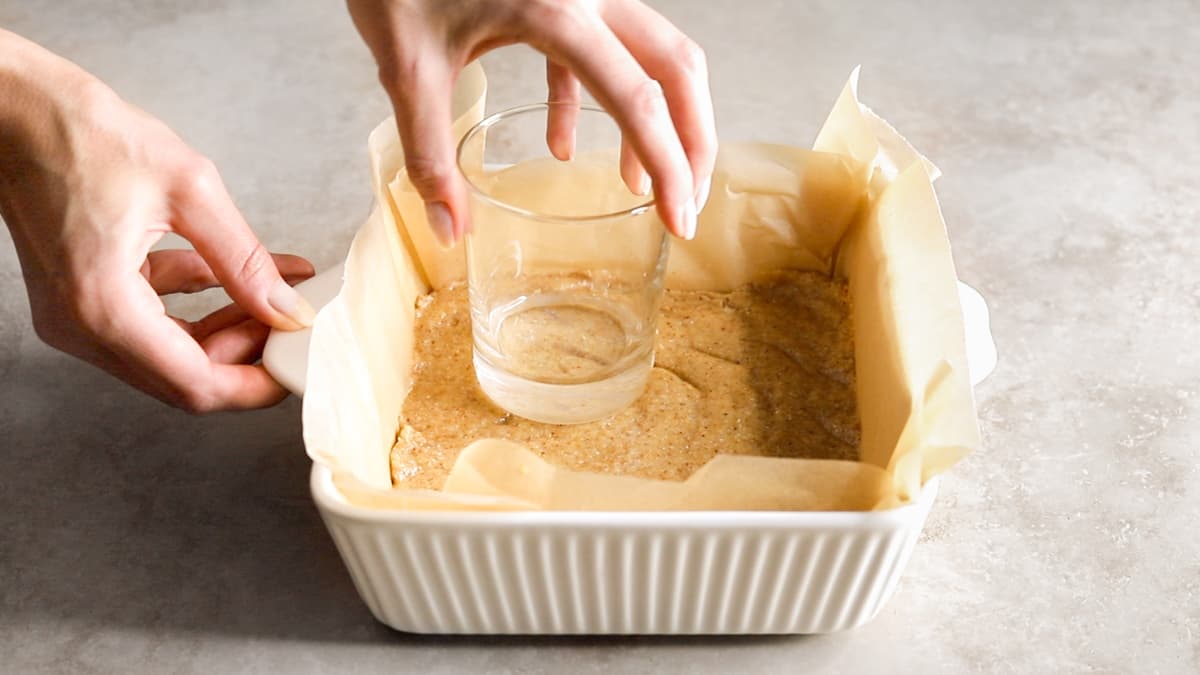 Pressing cheesecake biscuit base with glass in lined dish