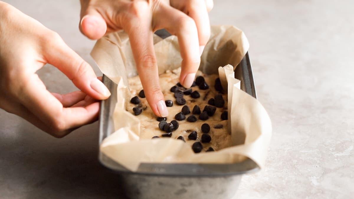 Cookie dough mixture pressed into a lined loaf pan with chocolate chips sprinkled on top