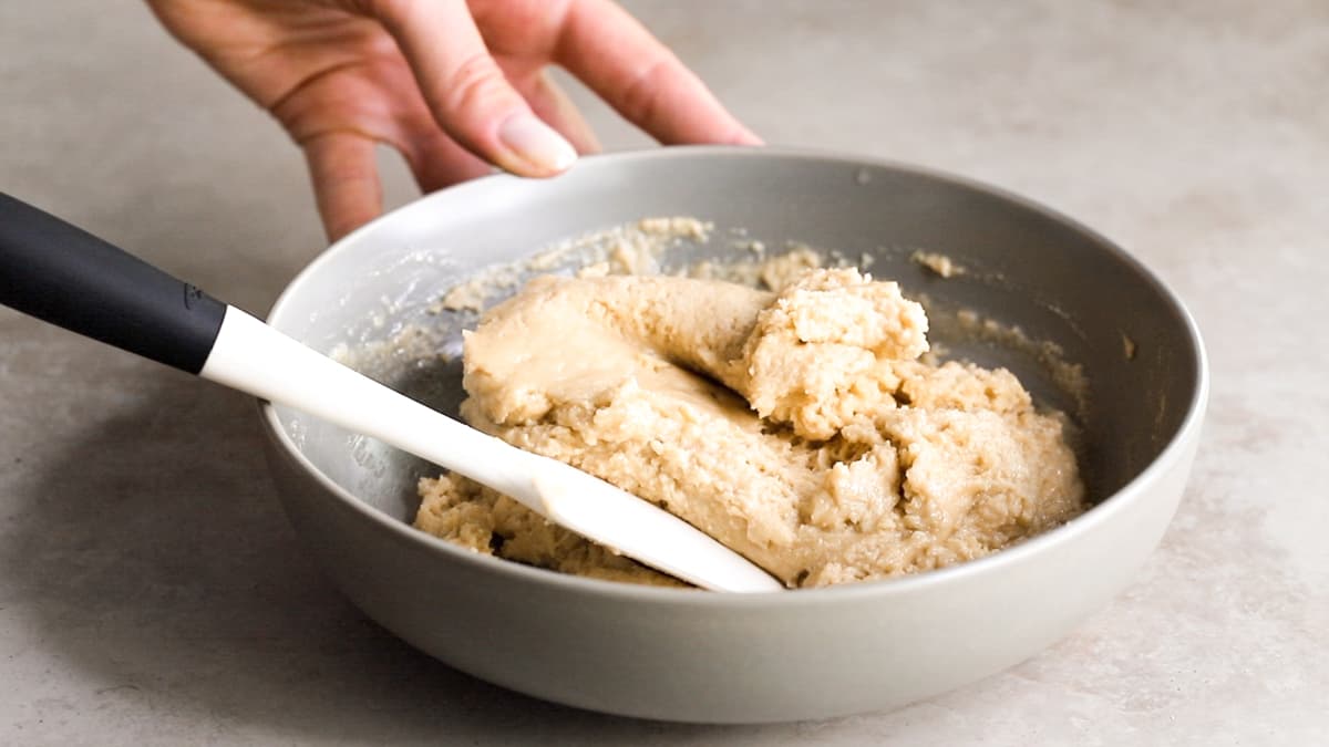 Bowl with cookie dough mixture of oats, protein powder, tahini, syrup, coconut oil, and vanilla