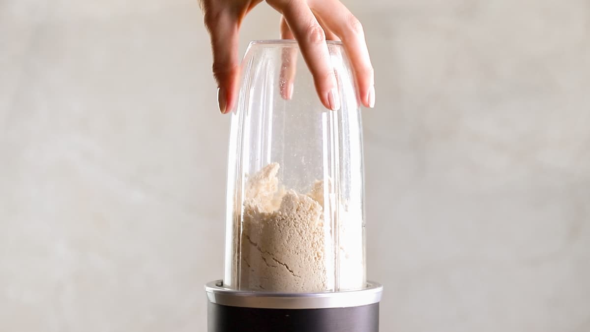 Blender containing rolled oats, desiccated coconut, and egg white protein powder being blended into a fine powder