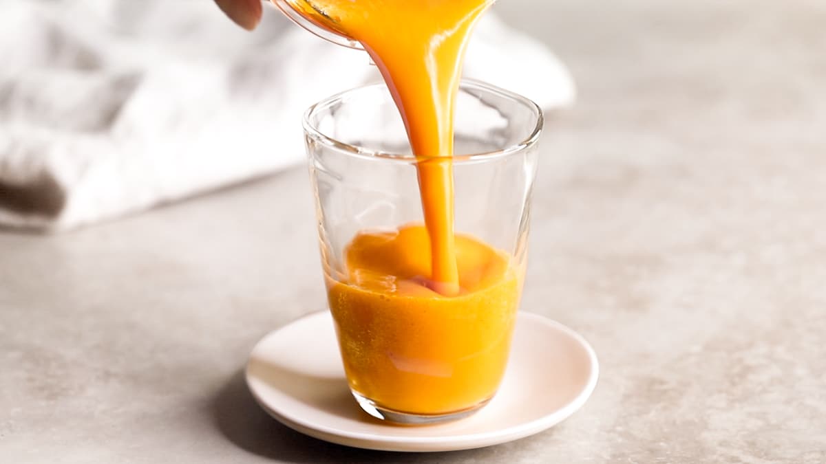 Pouring orange ginger carrot smoothie into a glass