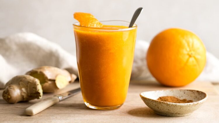 Orange ginger carrot smoothie in a glass on a wooden board