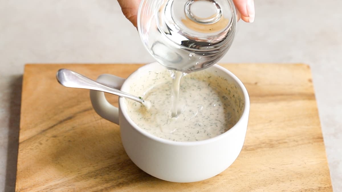 Creamy vegan tahini ranch dressing being thinned with water in a cup