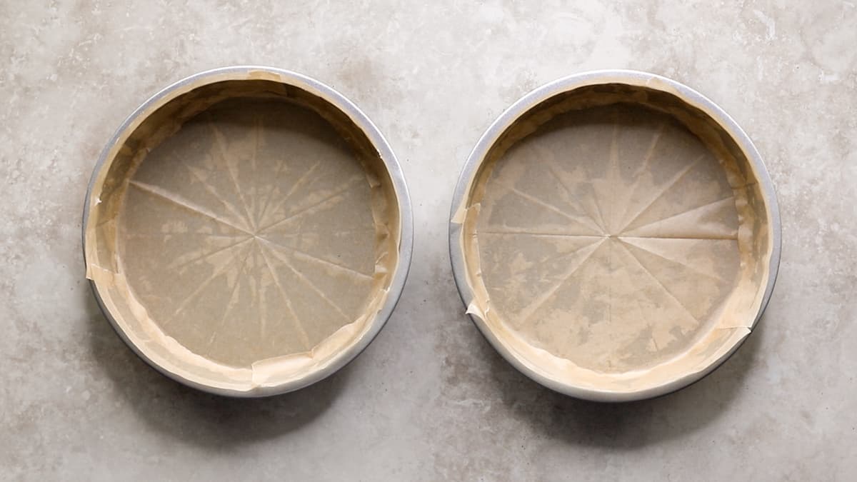 Two round cake tins lined with baking paper on a countertop