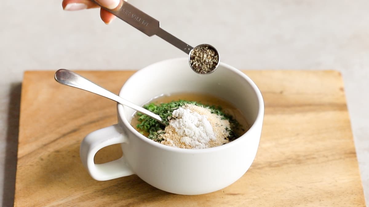 Cup of creamy vegan tahini ranch dressing with garlic, onion powder, vinegar, and mixed herbs