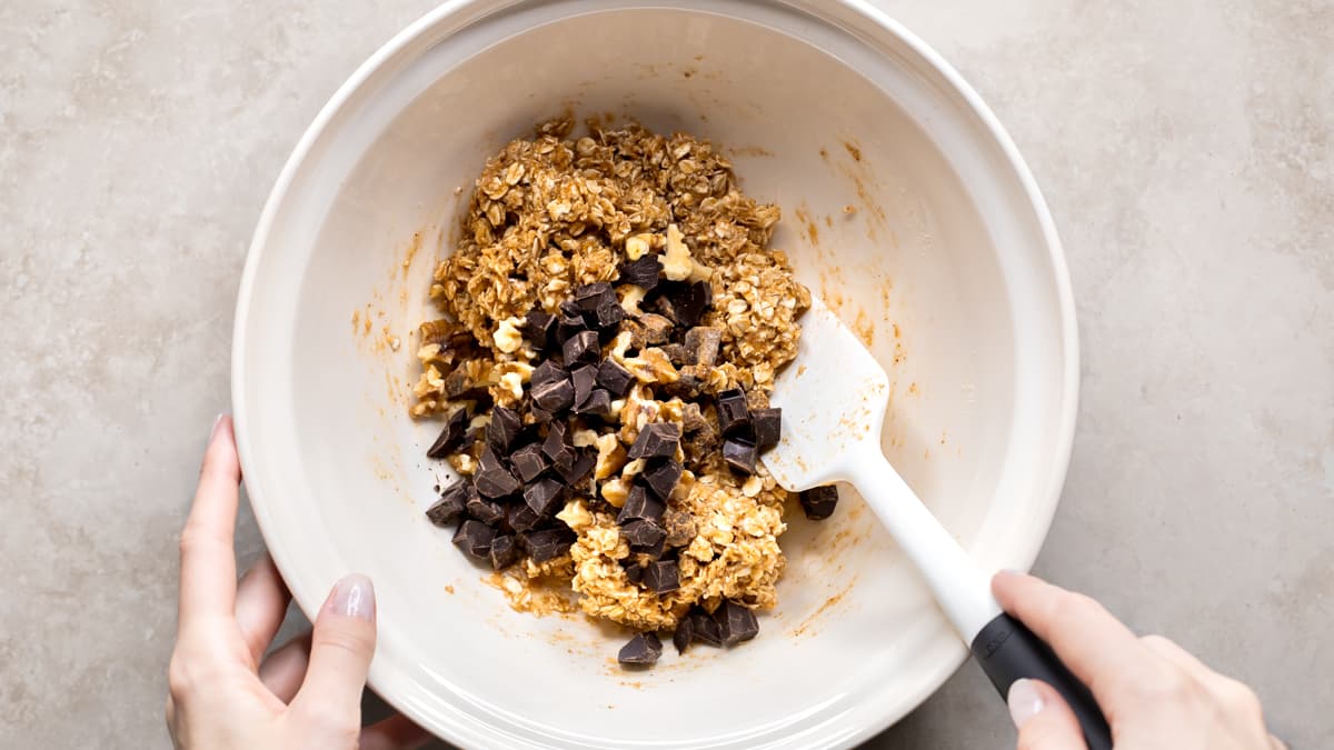 Bowl of oatmeal breakfast bar mixture with oats, almond butter, syrup, and mix-ins being stirred
