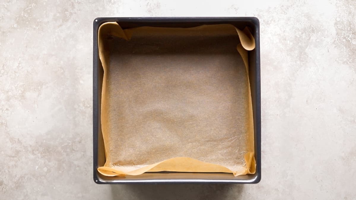 Square cake pan lined with baking paper ready for oatmeal bar mixture