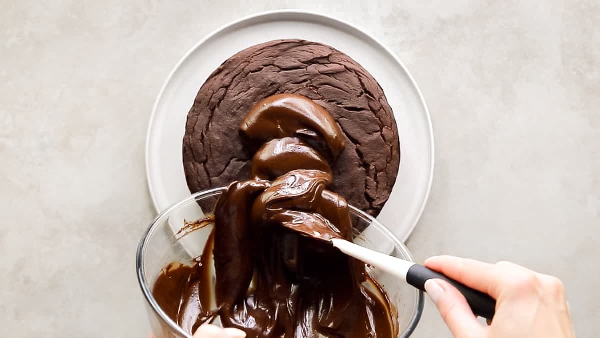 Pouring vegan avocado chocolate frosting onto chocolate cake with spatula