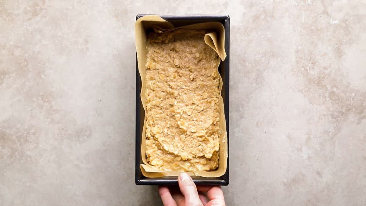 Smooth banana cinnamon oatmeal protein batter spread evenly in a lined loaf pan, ready for baking