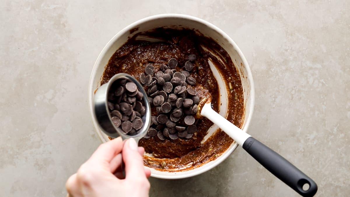 Adding chocolate chips to zucchini muffin batter in bowl