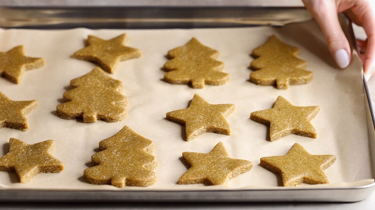 Gingerbread cookie dough cut into Christmas tree and star shapes on parchment paper