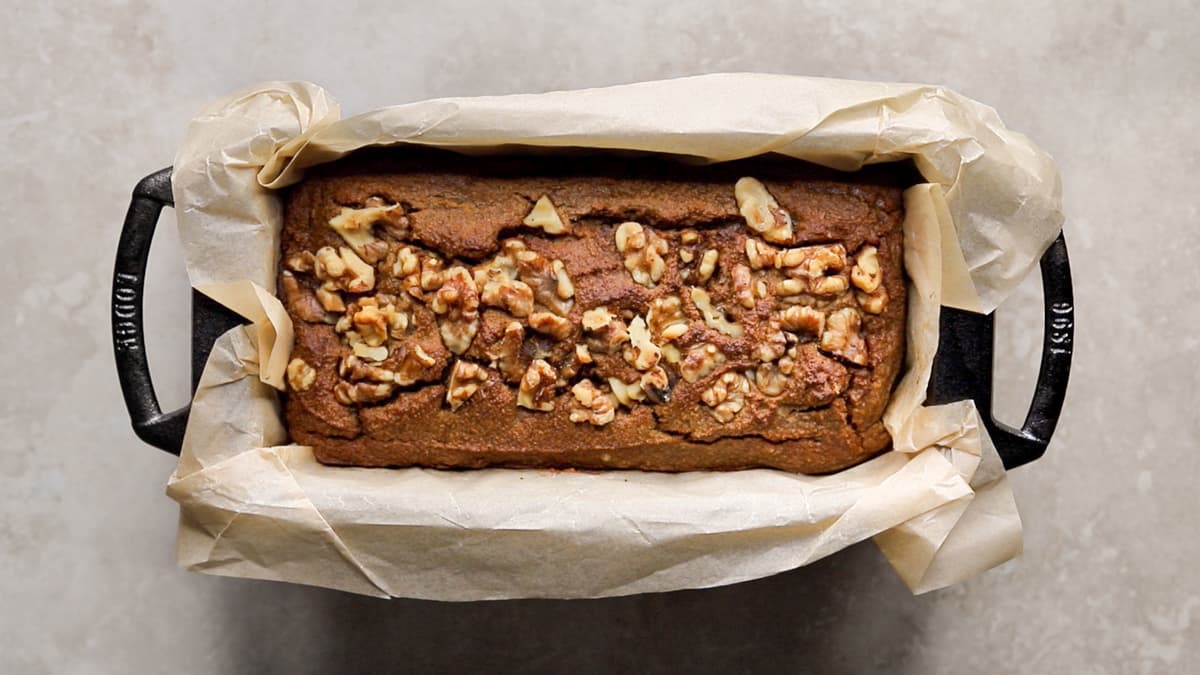 Freshly baked coconut flour banana bread in a loaf pan, golden brown on top with walnuts