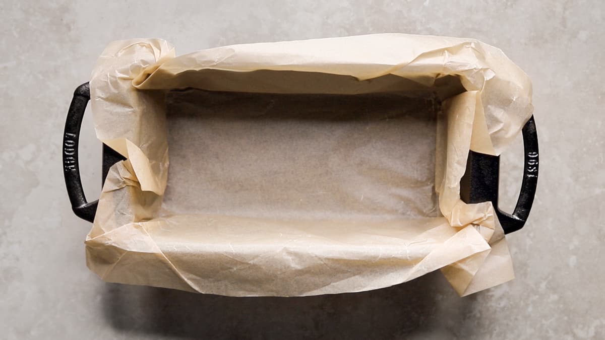A cast iron loaf pan lined with parchment paper, ready for batter