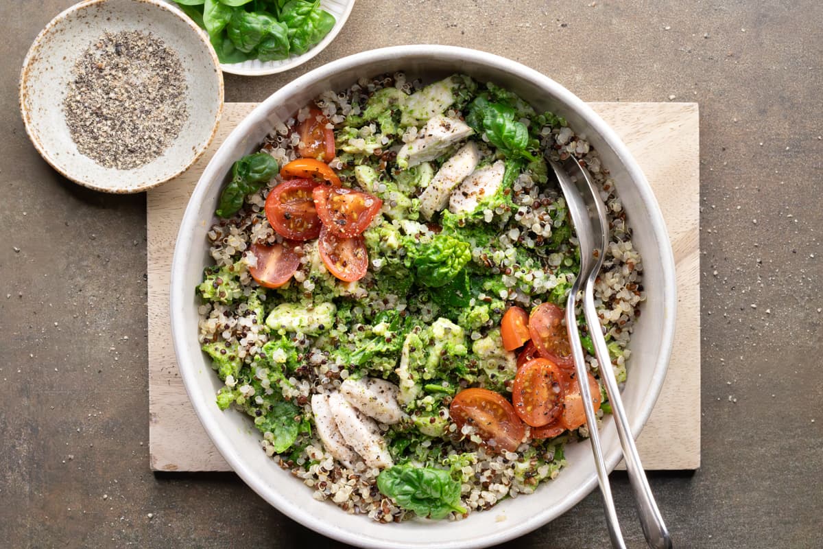 Healthy chicken quinoa salad in a bowl with tri-color quinoa, fresh greens, tomatoes, and pesto dressing