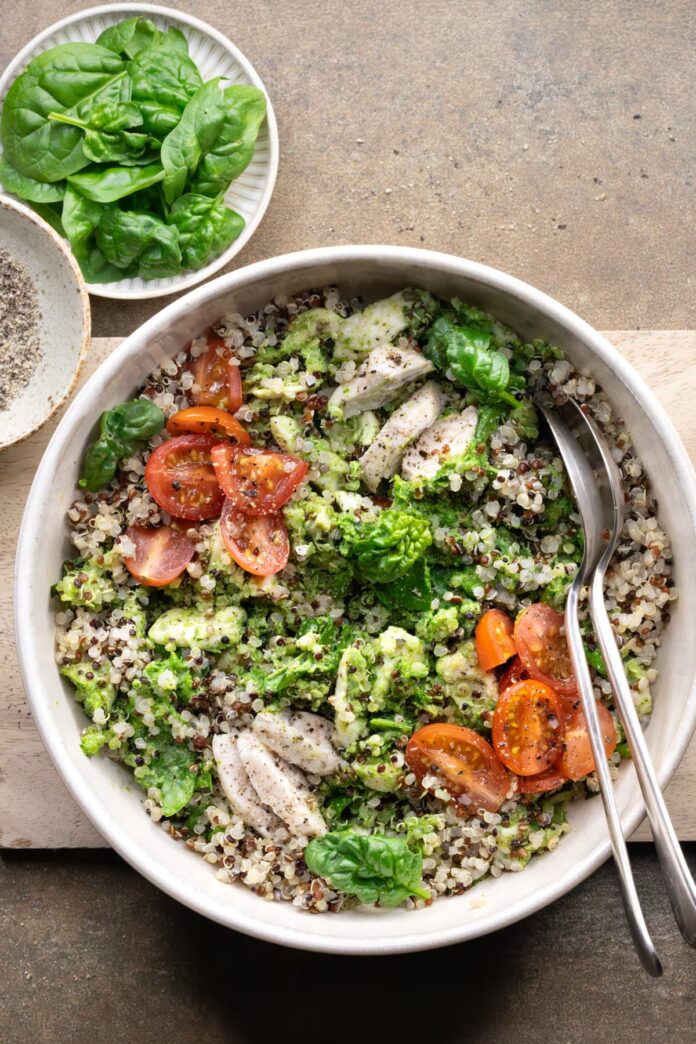 Chicken quinoa salad in a bowl with sliced chicken breast, baby spinach, grape tomatoes, and cashew pesto dressing