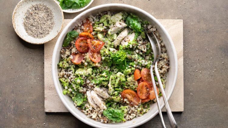 Chicken quinoa salad arranged in a bowl with colorful vegetables, quinoa, chopped chicken and pesto dressing