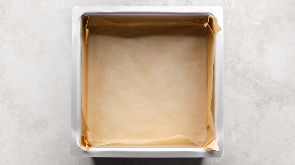 Line the base and sides of a square cake pan with parchment paper