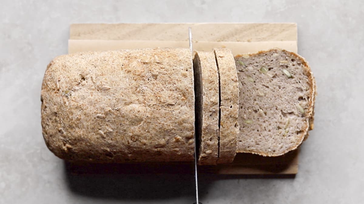 Baked bread loaf being sliced on a wooden cutting board