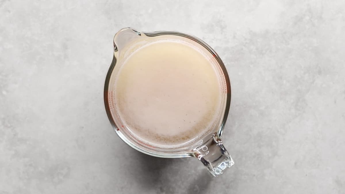 Yeast, sugar, and warm water mixed in a jug with a foamy layer forming on top
