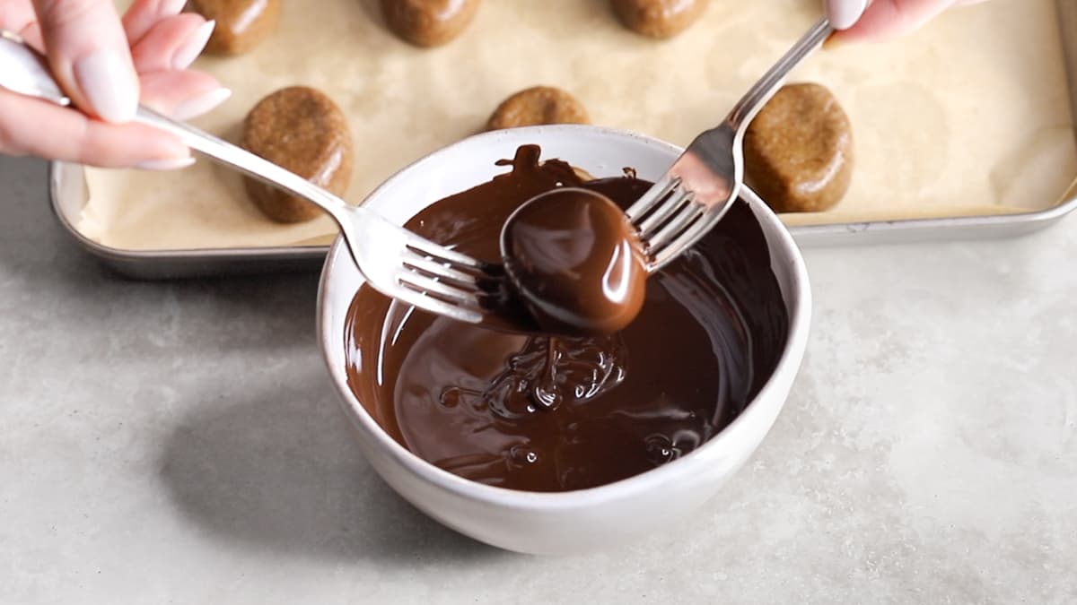 An almond butter Easter egg held between two forks, being dipped into melted chocolate in a bowl