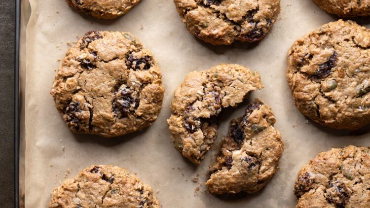 Baked flourless oatmeal raisin cookies on a tray with one cookie broken in half