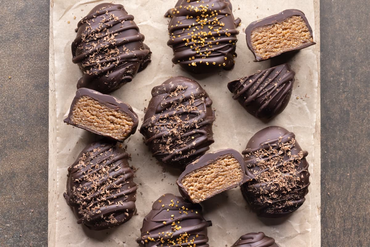 A mix of whole and halved chocolate Easter eggs on a parchment-lined board, showing the spiced almond butter filling in the halved eggs