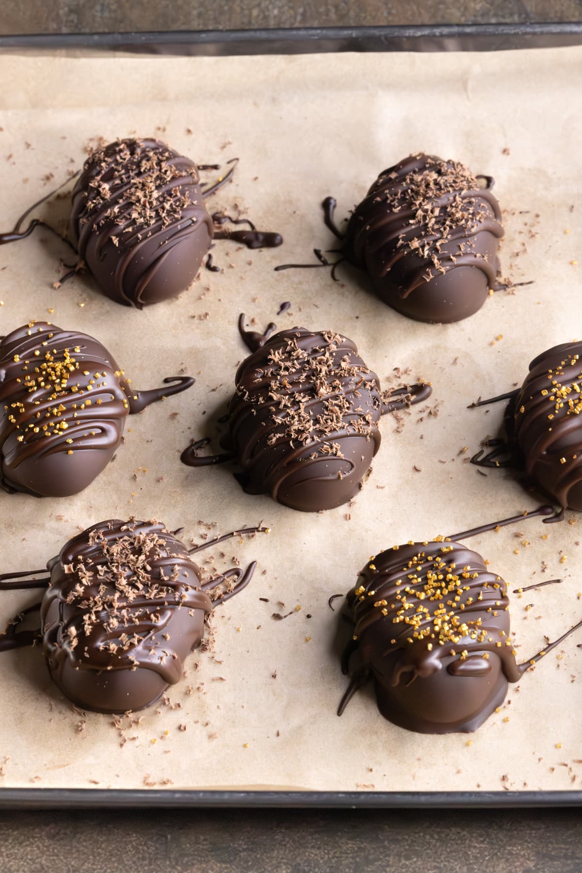 Homemade chocolate Easter eggs decorated with grated chocolate and gold sprinkles on a parchment-lined tray