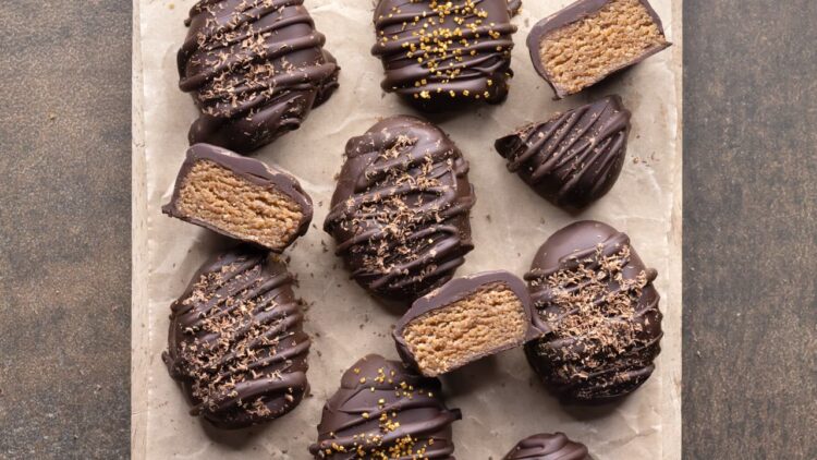 Whole and halved spiced chocolate almond butter Easter eggs on a parchment-lined wooden board