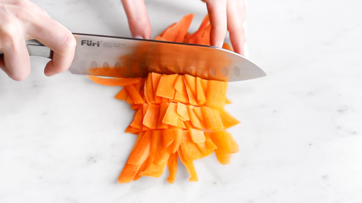 Carrot ribbons being cut into bite-sized pieces with a large knife