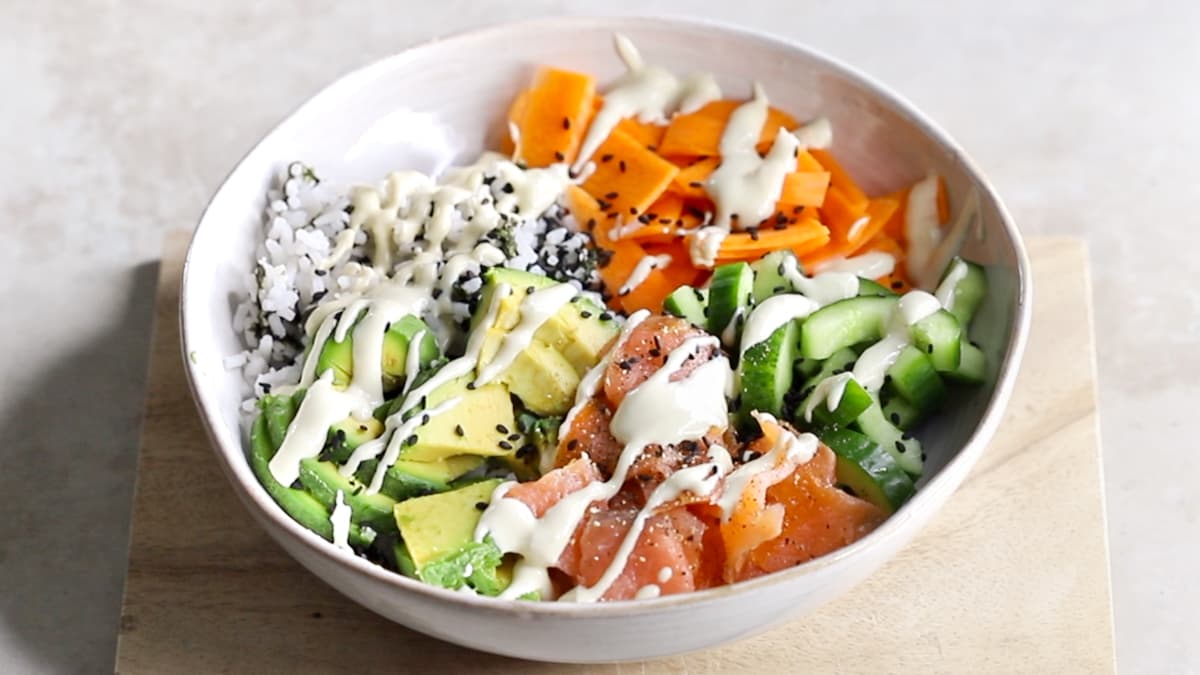 Finished smoked salmon rice bowl with white rice, nori, avocado, vegetables, black sesame seeds, and wasabi dressing