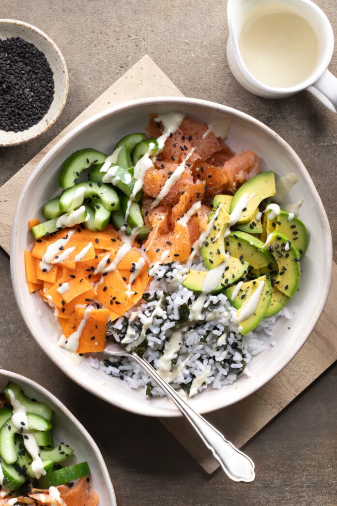 Smoked salmon rice bowl served with avocado, vegetables, black sesame seeds, and wasabi dressing