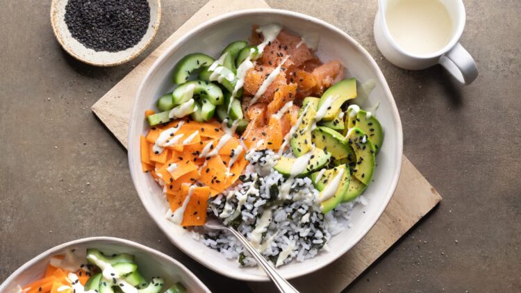 Smoked salmon rice bowl with avocado, nori, vegetables, black sesame seeds, and a drizzle of wasabi dressing