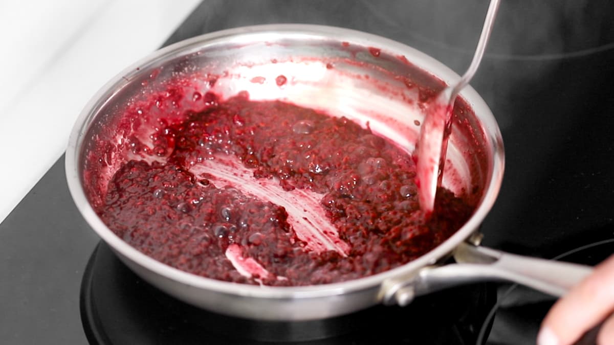 Thickened raspberry compote being stirred with a spoon in a saucepan