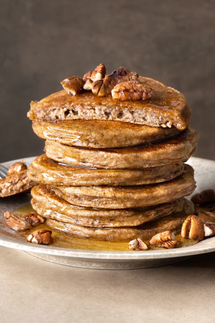 A stack of banana cottage cheese pancakes served with chopped pecans and brown rice syrup
