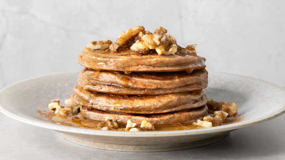 A stack of banana cottage cheese pancakes served with chopped walnuts and brown rice syrup