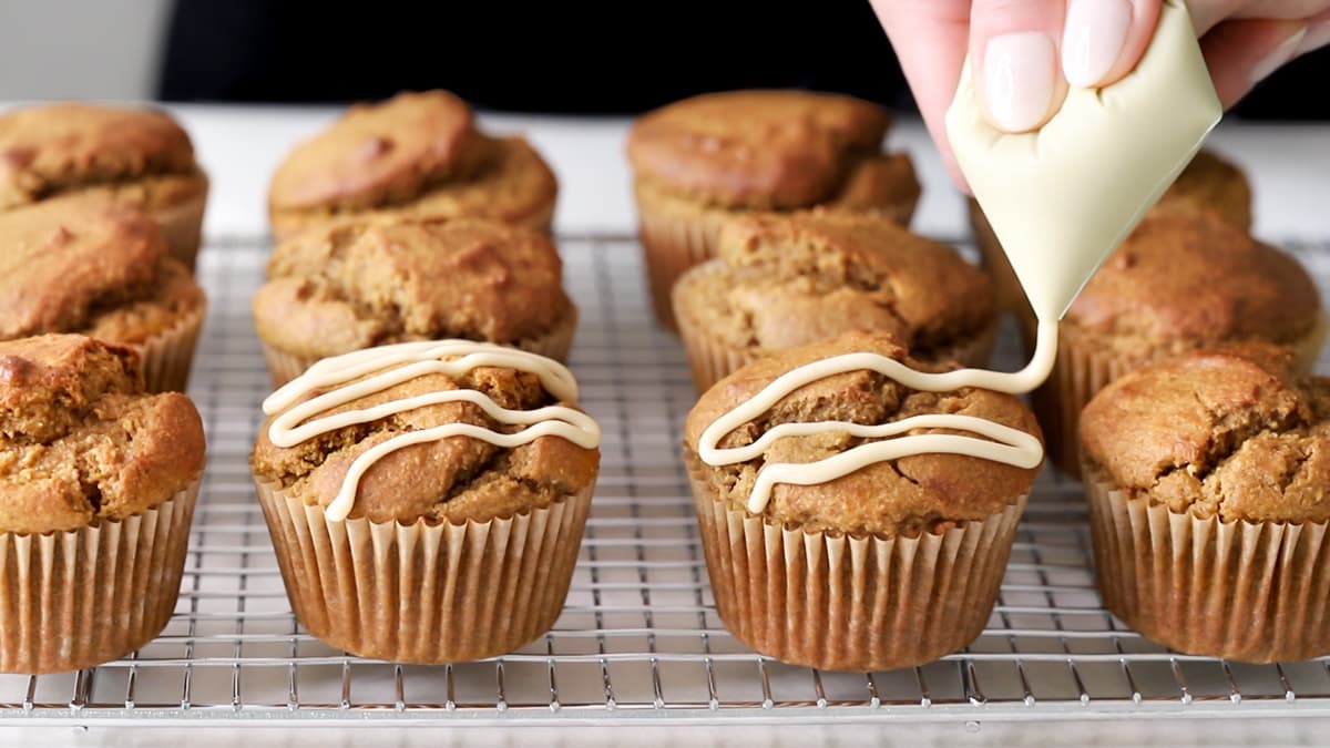 Maple glaze being piped over pumpkin muffins on a cooling rack