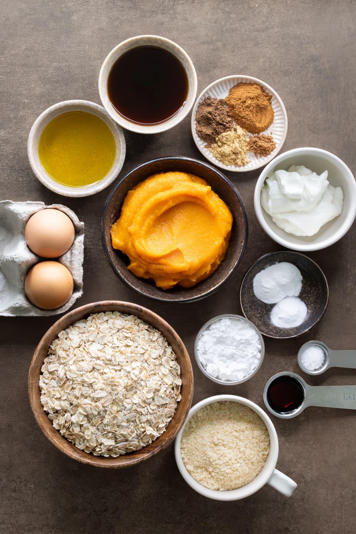 Ingredients for pumpkin oat muffins set out in bowls, cups, and measuring spoons